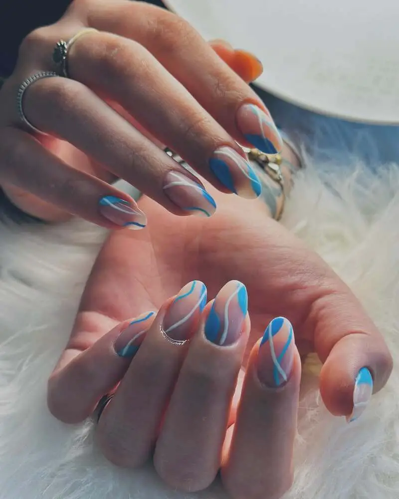 Abstract light blue nails with white wavy patterns on a nude base