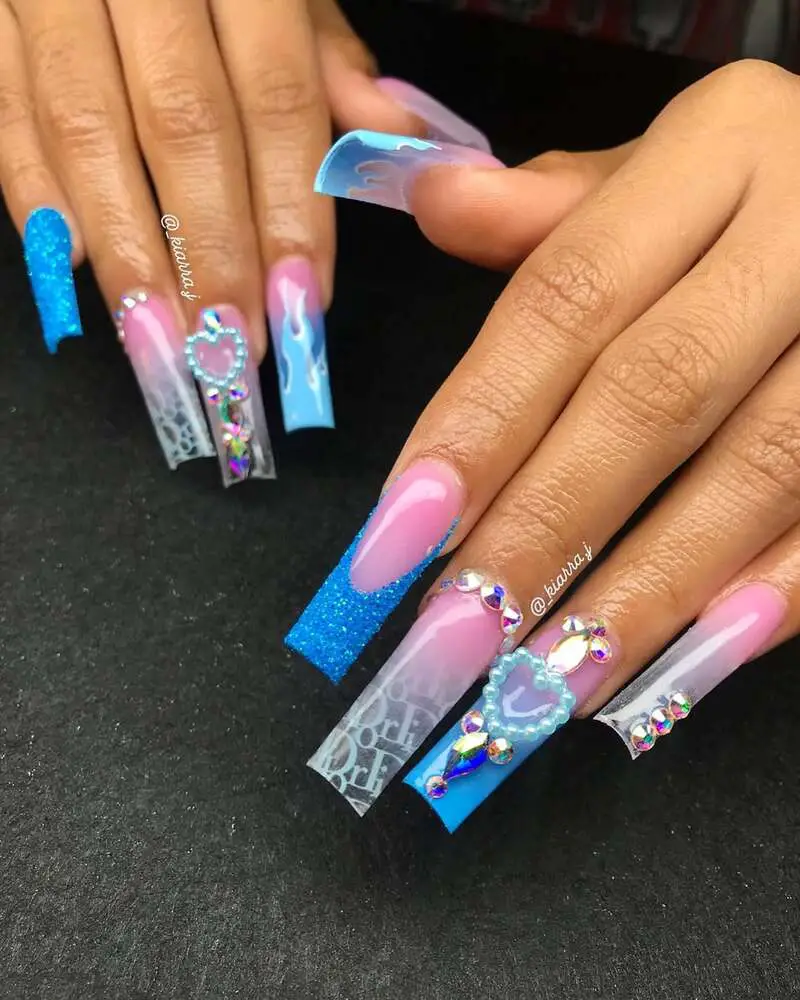 Long nails featuring blue glitter, pink gradients, crystal embellishments, and heart-shaped decorations