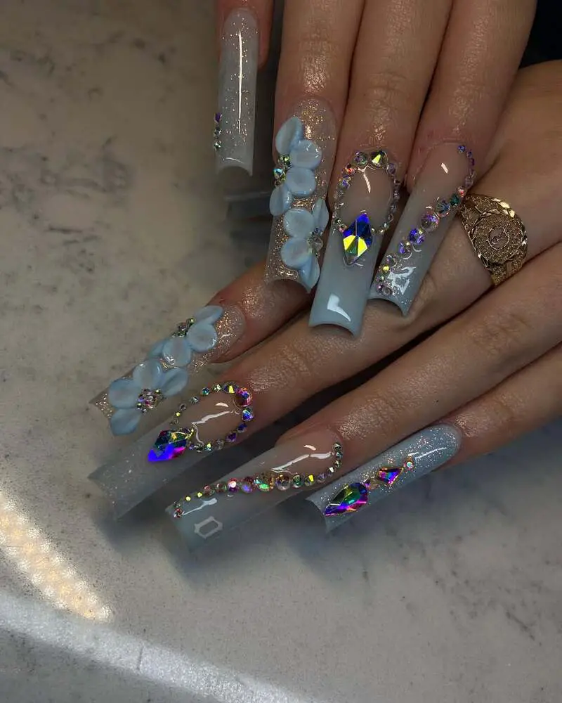 Long nails with blue flowers, holographic crystals, and rhinestone decorations on grey-blue base