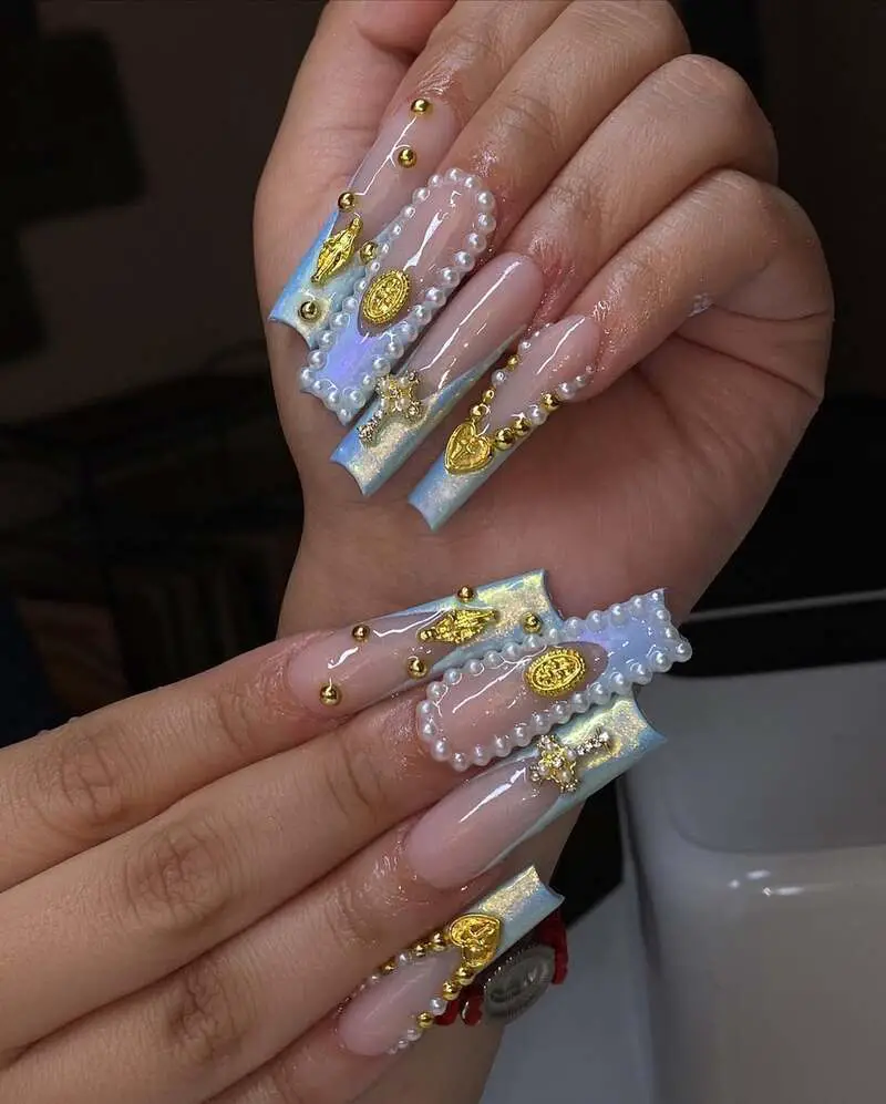 Long nails with iridescent blue tips decorated with pearl borders, gold charms, and metallic studs