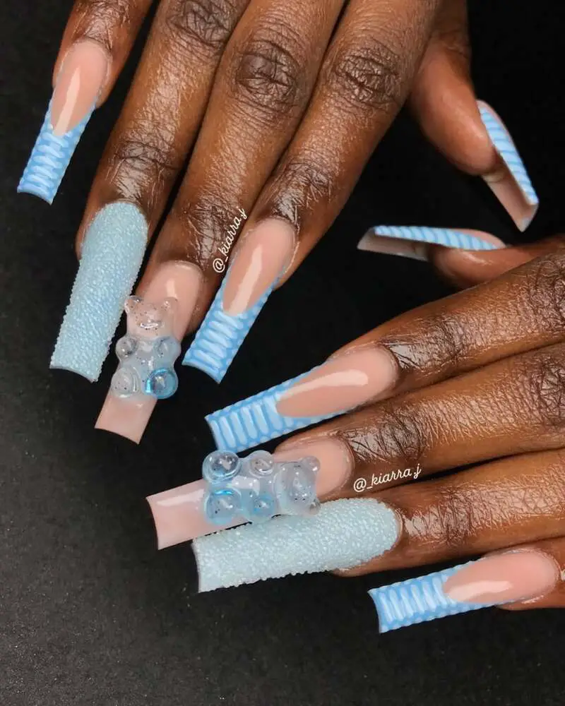 Long square nails featuring blue striped tips, a sugar texture, and 3D gummy bear decorations on a nude base